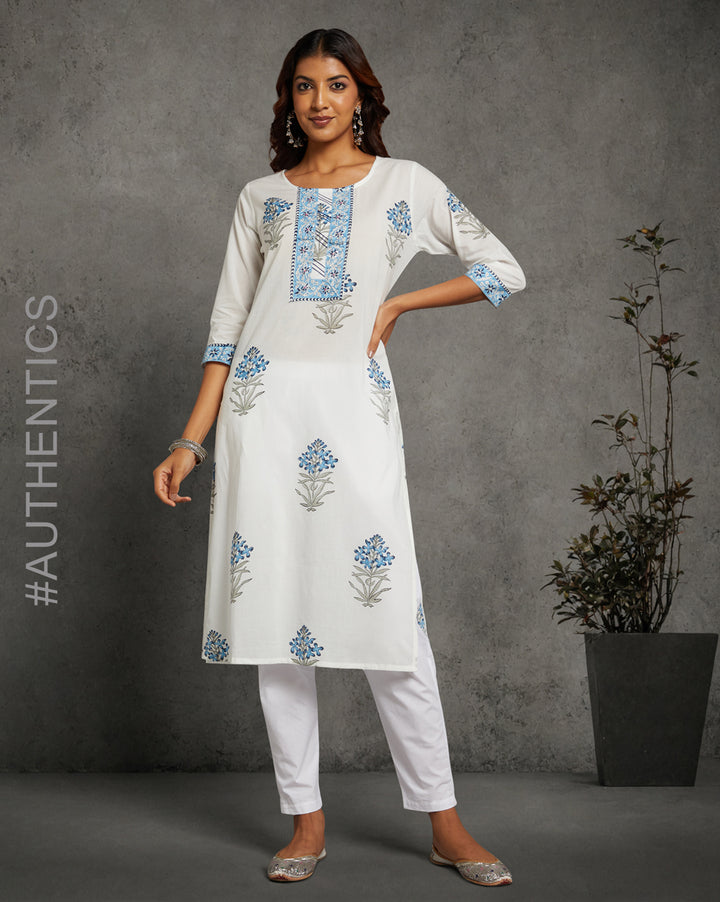 Stylish White Round Neck Hand Block Cotton Kurti,paired with white pant and jutti, worn by a woman standing next to flowerpot.
