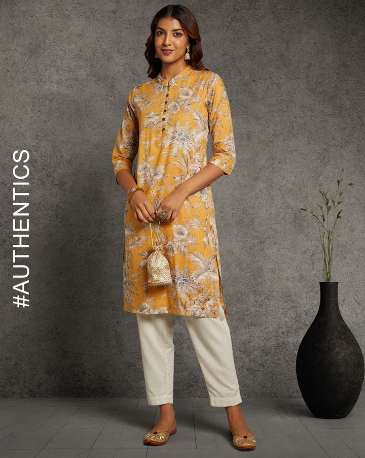 Stylish Yellow Collar Neck Hand Block Cotton Kurti, paired with white wide pant and jutti, worn by a woman standing next to flowerpot.
