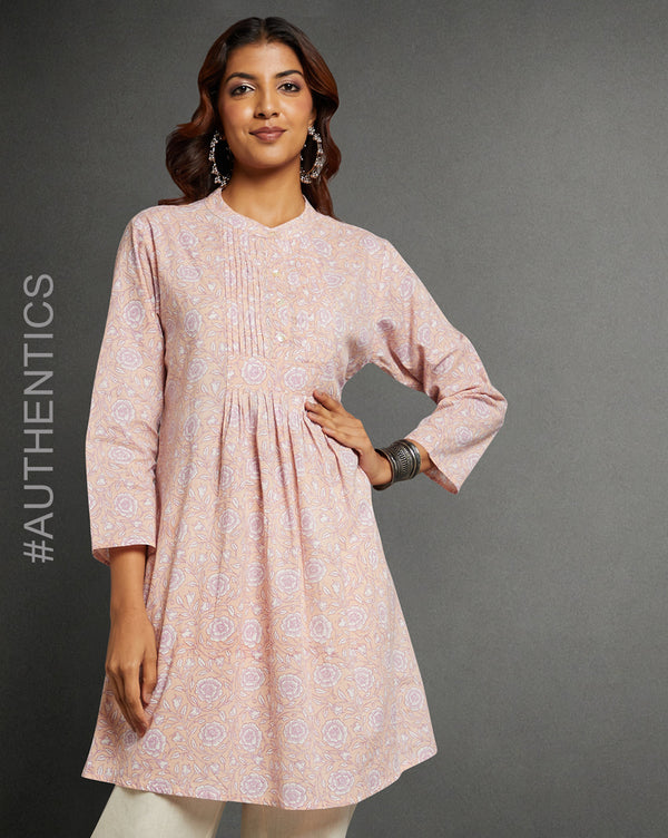 Stylish Pink Floral Print Cotton A-Line Kurta, paired with white pant and jutti, worn by a woman standing next to a flowerpot.
