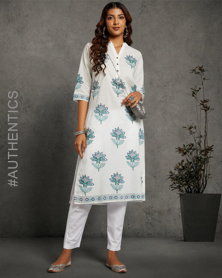 Stylish White Cotton Straight Kurta with Chinese Collar and V-Neck, paired with white pant and jutti, worn by a woman standing next to a flowerpot.


