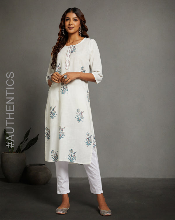 Stylish White Cotton Straight Kurta with round Neck, paired with white pant and jutti, worn by a woman standing next to a flowerpot.
