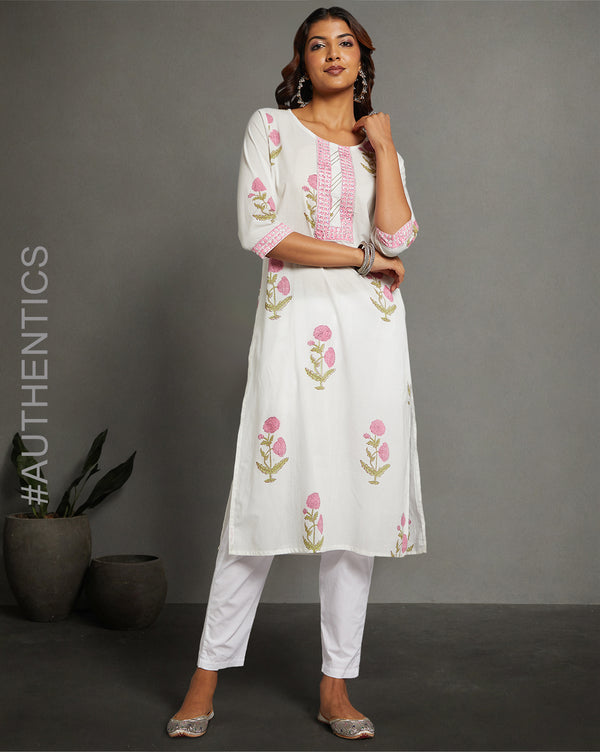 Stylish  White Round Neck and Hand Block floral print Cotton Kurti, paired with white wide pant and jutti, worn by a woman standing next to flowerpot.
