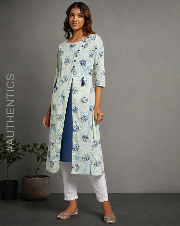 Stylish White and blue Cotton A-line Kurti with Round Neck, paired with white pant and jutti, worn by a woman standing next to a flowerpot.
