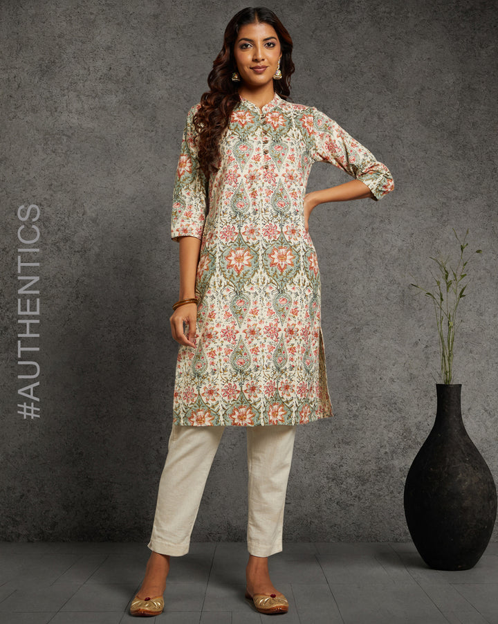 Stylish Yellow color floral print kurti, paired with white pant and jutti, worn by a woman standing next to flowerpot.
