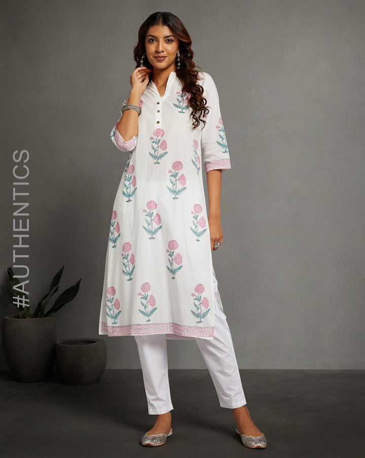 Stylish White V Neck Hand Block Cotton Kurti, Sky Blue Floral Hand Block Cotton Kurta, paired with white pant and jutti, worn by a woman standing next to flowerpot.
