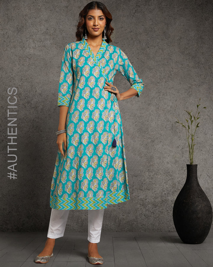 Stylish blue Cotton printed Angrakha Kurta with V-Neck, paired with white pant and jutti, worn by a woman standing next to a flowerpot.