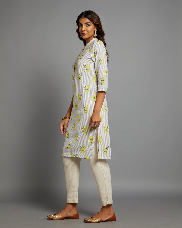 Side profile of a woman wearing a Sunny Yellow Floral Hand Block Cotton V-Neck Kurta with three-quarter sleeve paired with off white pant and jutti, showcasing the kurti's length and the smooth drape over the body