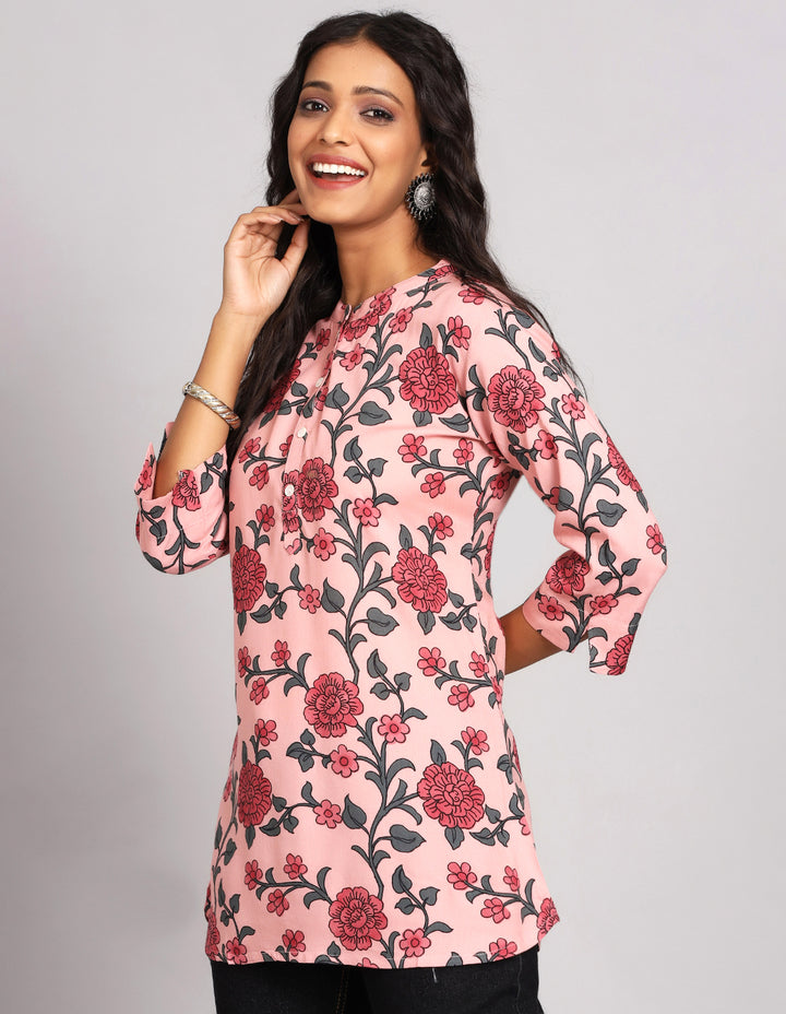 Side profile of a woman wearing Chalk Pink floral printed Short Kurti with three-quarter sleeve paired with black jeans and brown slippers,showcasing the kurti's length and the smooth drape over the body