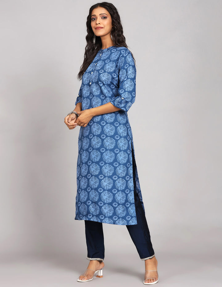 Side profile of a woman wearing a Blue Long Kurti with Collar Neck Line with three-quarter sleeve paired with navy blue pant and white transparent sandals, showcasing the kurti's length and the smooth drape over the body