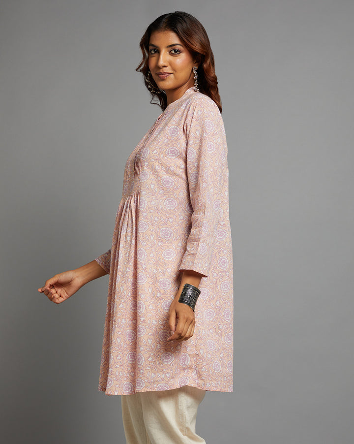 Side profile of a woman wearing Pink Floral Print Cotton A-Line Kurta with Round Neck with three-quarter sleeve paired with white pant and jutti, showcasing the kurti's length and the smooth drape over the body


