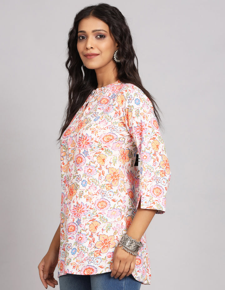 Side profile of a woman wearinga Floral Cream color Short Kurti with Collar Neck line and three-quarter sleeve paired with blue skinny jeans and brown sandals, showcasing the kurti's length and the smooth drape over the body