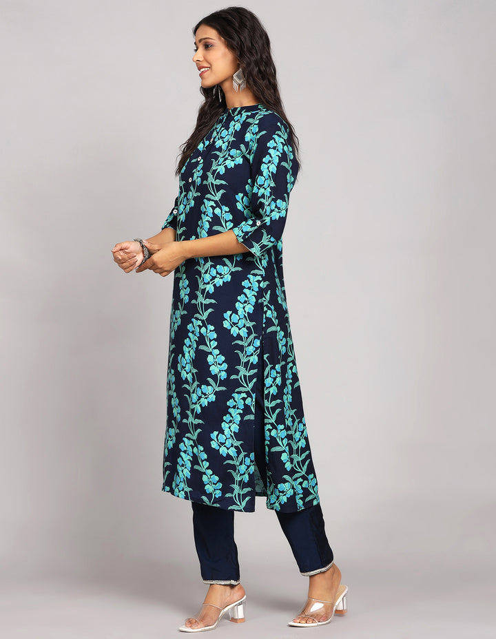 Side profile of a Navy Blue Floral Printed Long Kurti with Collar Neck Line with blue pant and three fourth sleeves with transparent sandals, showcasing the kurti's length and the smooth drape over the body