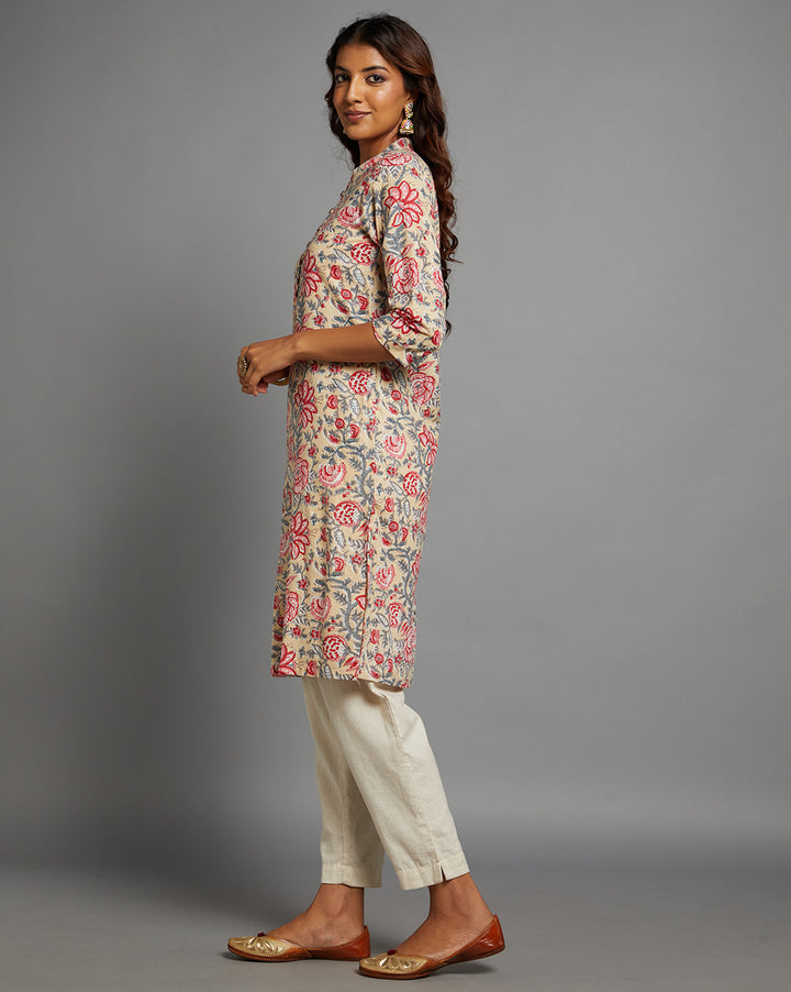 Side profile of a woman wearing a beige yellow floral printed kurti with collar neck and wooden button design with three-quarter sleeve paired with white pant , showcasing the kurti's length and the smooth drape over the body