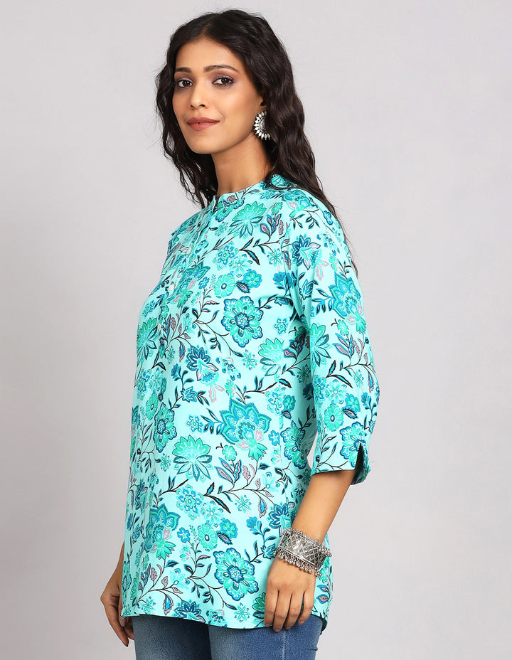 Side profile of a woman wearinga  Aqua Green Short Kurti with Floral Print and three-quarter sleeve paired with blue skinny jeans and brown sandals, showcasing the kurti's length and the smooth drape over the body