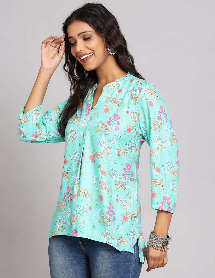 Side profile of a woman wearing a  Aqua Blue Floral Print Short Kurti with three-quarter sleeve paired with blue skinny jeans and brown sandals,showcasing the kurti's length and the smooth drape over the body