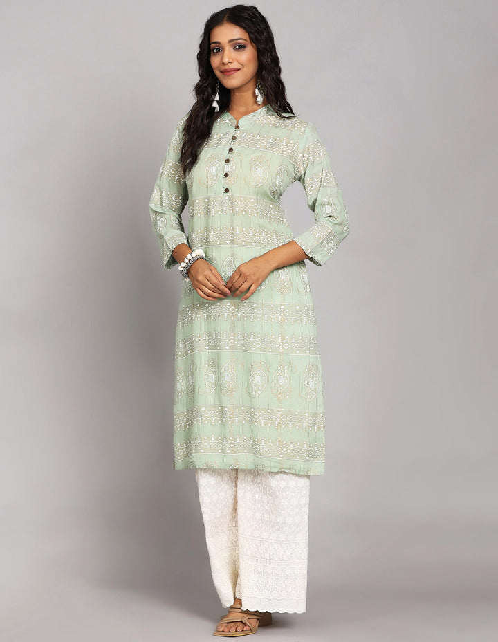 Side profile of a woman wearing Mint Green Long Kurti with collar neckline with three-quarter sleeve paired with white palazzo and brown sandals, showcasing the kurti's length and the smooth drape over the body