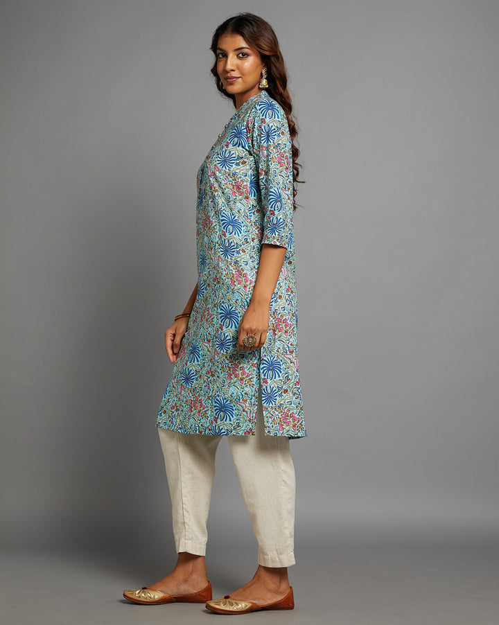 Side profile of a woman wearing a Sky blue floral printed kurta, paired with white pant and three-fourth sleeve, showcasing the kurti's length and the smooth drape over the body