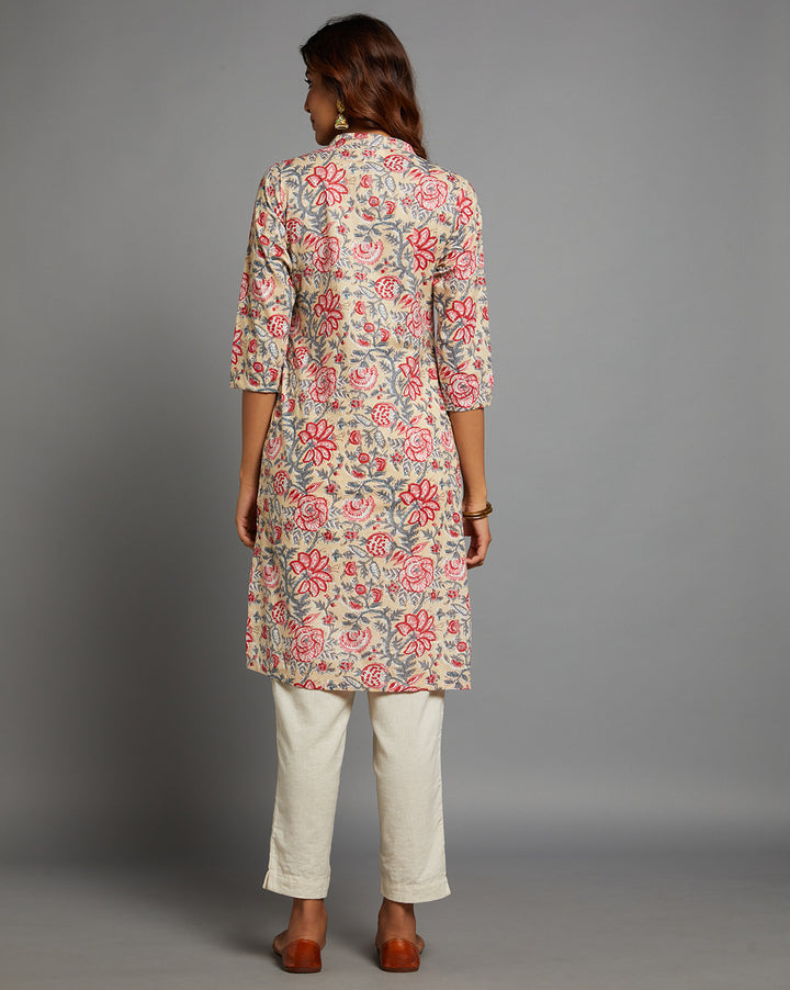 Woman showing the back view of a beige yellow floral printed long kurti with three-quarter sleeve paired with white pant and brown jutti, highlighting the relaxed fit and simple design from behind.
