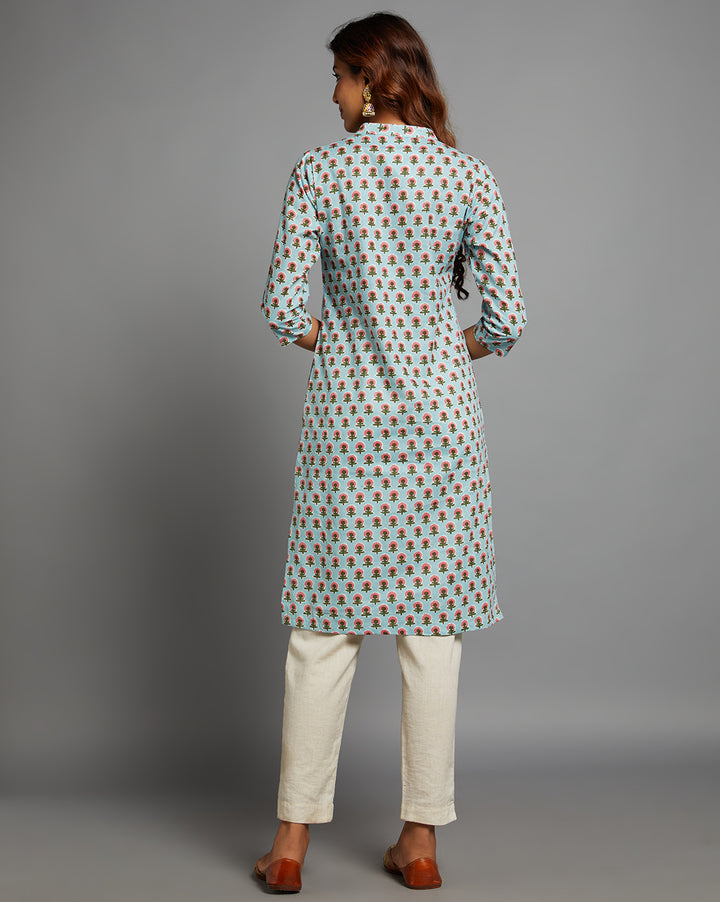 Woman showing the back view of a Sky Blue Floral Hand Block Cotton Kurti,  with three-quarter sleeve paired with white pant and jutti, highlighting the relaxed fit and simple design from behind.
