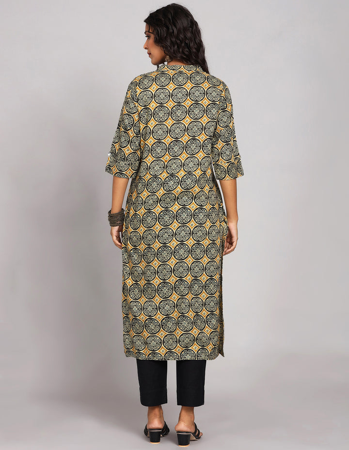 Woman showing the back view of a   Rust Yellow Kurti with hand block Print and three-quarter sleeve, paired with  black pant and balck heels,highlighting the relaxed fit and simple design from behind.
