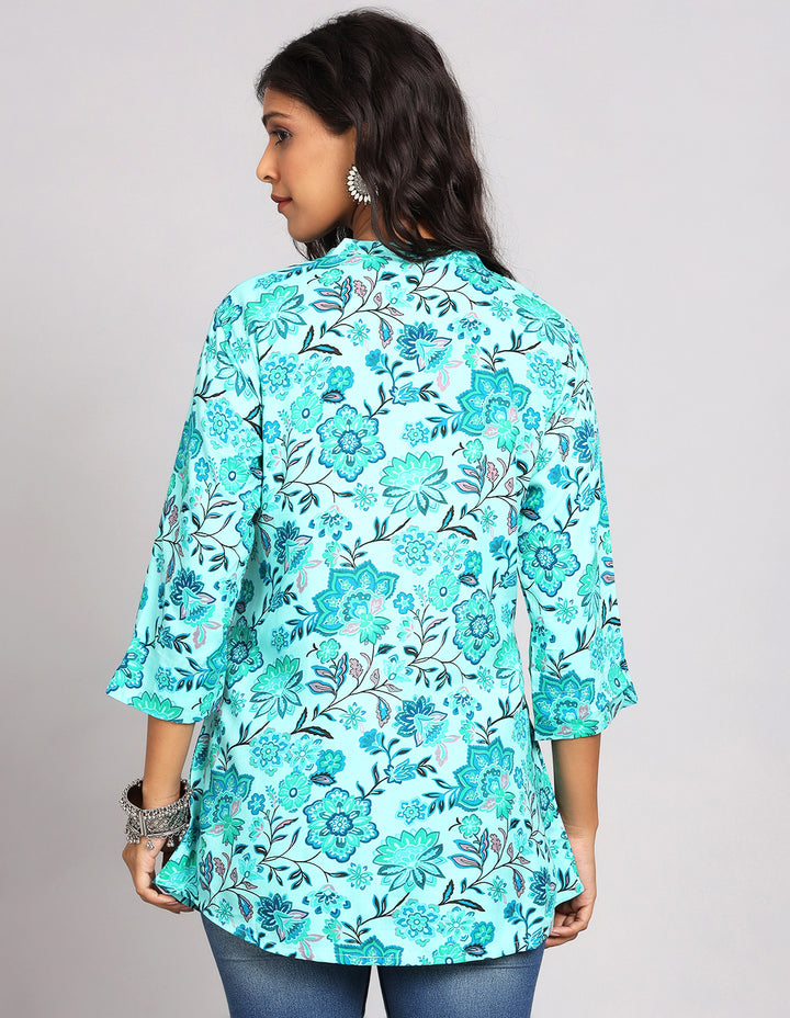 Woman showing the back view of Aqua Green Short Kurti with Floral Print and three-quarter sleeve paired with blue skinny jeans and brown sandals, highlighting the relaxed fit and simple design from behind.