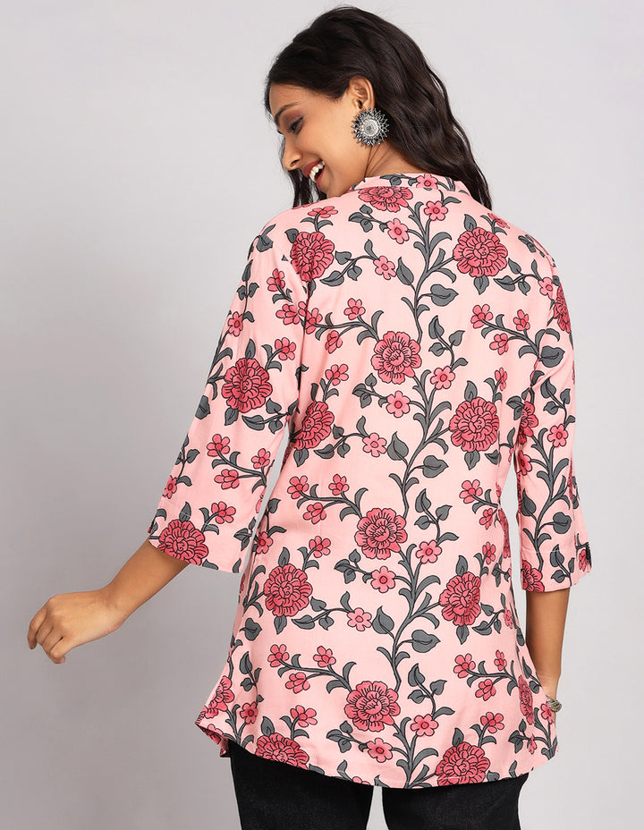 Woman showing the back view of a Chalk Pink floral printed Short Kurti with three-quarter sleeve paired with black jeans and brown slipeers, highlighting the relaxed fit and simple design from behind.