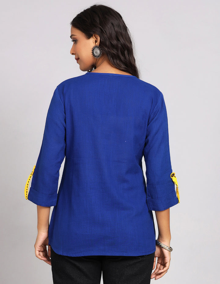 Woman showing the back view of a royal blue three-quarter sleeve with yellow strips top paired with black skinny jeans, highlighting the relaxed fit and simple design from behind.