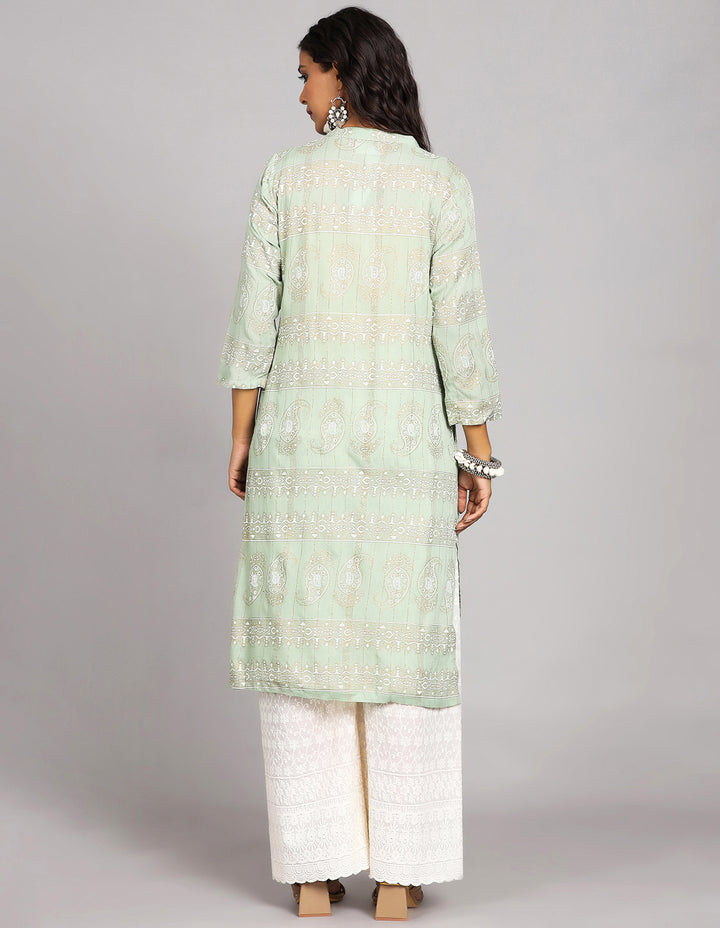 Woman showing the back view of a  Mint Green Long Kurti and three-quarter sleeve, paired with white palazzo and brown heels, highlighting the relaxed fit and simple design from behind.