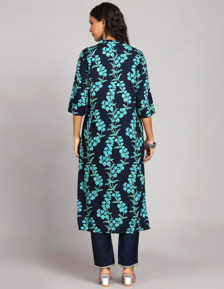 Woman showing the back view of Navy Blue Floral Printed Long Kurti with Collar Neck Line with blue pant and white transparent sandals, highlighting the relaxed fit and simple design from behind.


