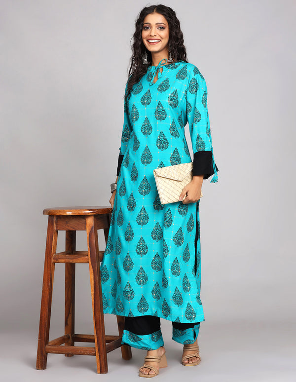 Stylish Printed Blue Color Cotton Knee Length Kurta, paired with brown heels, worn by a woman standing next to a table with open hair and taking white handbag.