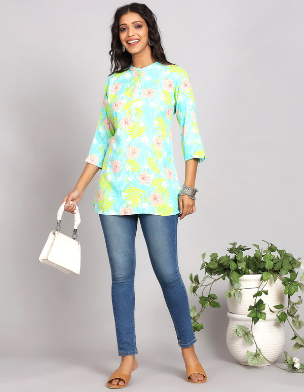 Stylish Sky Blue Short Kurti with Collar Neck line, paired with blue skiny jeans and brown sandals, worn by a woman standing next to a flowerpot taking a white handbag in hands.