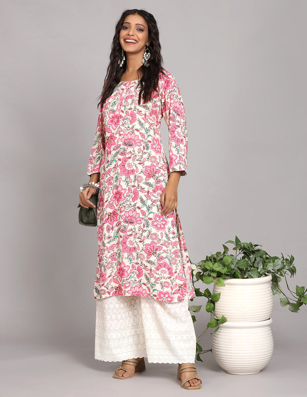 Stylish white color long kurti with floral print, paired with white palazzo and brown heeled sandals, worn by a woman standing next to Flowerpot with a handbag.