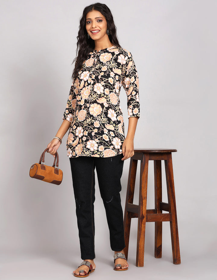 Stylish printed black floral print kurti,paired with black jeans and brown slippers, worn by a woman standing next to a Stool.