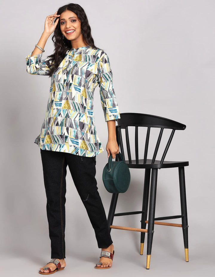 Stylish Printed Grey color Short Kurti, paired with black jeans and brown slippers, worn by a woman standing next to a Chair.