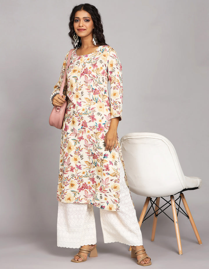 Stylish Cream Yellow Floral Printed Long Kurti with Round Neck Design, paired with white palazzo and brown heels, worn by a woman standing in white chair with open hair.