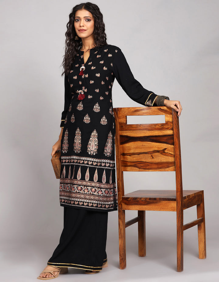 Stylish Black Palazzo Set With Hand Block Print, paired with brown heels, worn by a woman standing next to chair with open hair.

