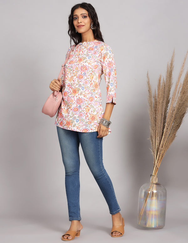 Stylish Floral Cream color Short Kurti with Collar Neck line, paired with blue skiny jeans and brown sandals, worn by a woman standing next to a flowerpot .