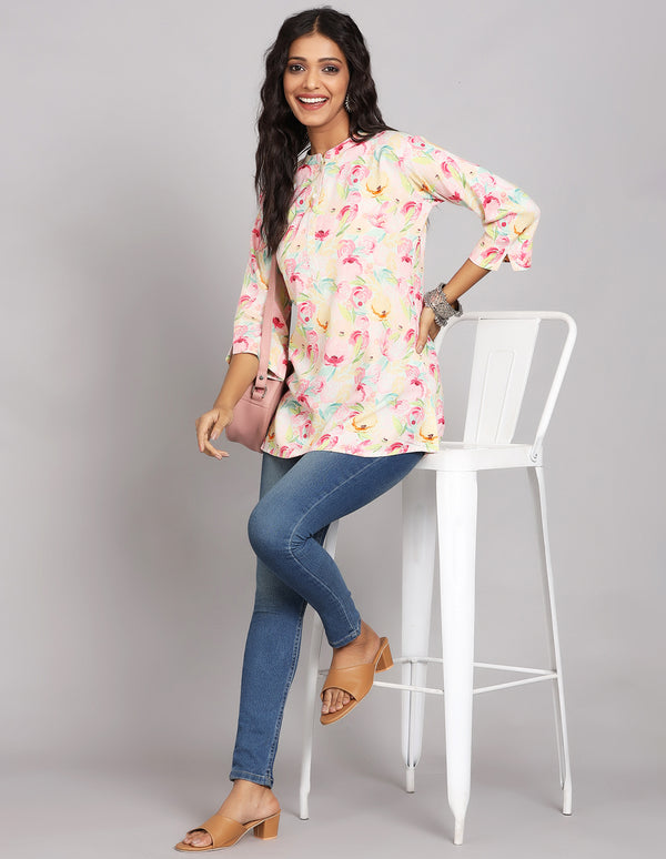 Stylish Multicolor Pastel Printed Short Kurti with Collar Neck Line, paired with blue skinny jeans and brown sandals, worn by a woman standing next to a white chair.