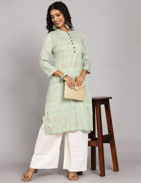 Stylish Mint Green Long Kurti, paired with white palazzo and brown heels, worn by a woman standing next to a table with a handbag and open hair.