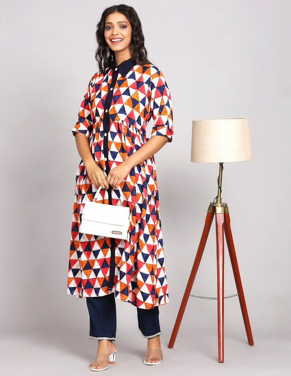 Stylish Multicolor Printed Long Kurti with Collor Neck Design, paired with navy blue pant with white transparent heels, worn by a woman standing next to a lamp with open hair.
