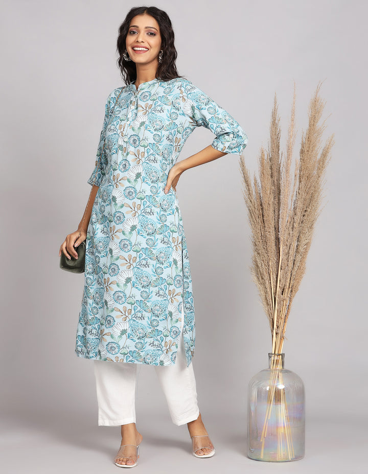 Stylish Blue and Grey color Long Kurti with Collar Neck Line with white pant and white transparent sandals, worn by a woman standing next to flowerpot.