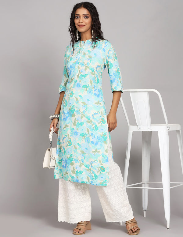 Stylish Blue color Long Kurti with collar Neck design, paired with white palazzo and brown heels, worn by a woman standing next to a chair with a handbag and open hair.
