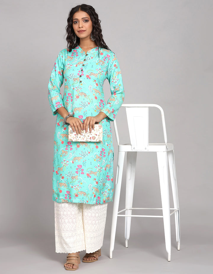 Stylish Aqua Green printed long kurti, paired with white wide leg palaazo and brown sandals, worn by a woman standing next to chair.