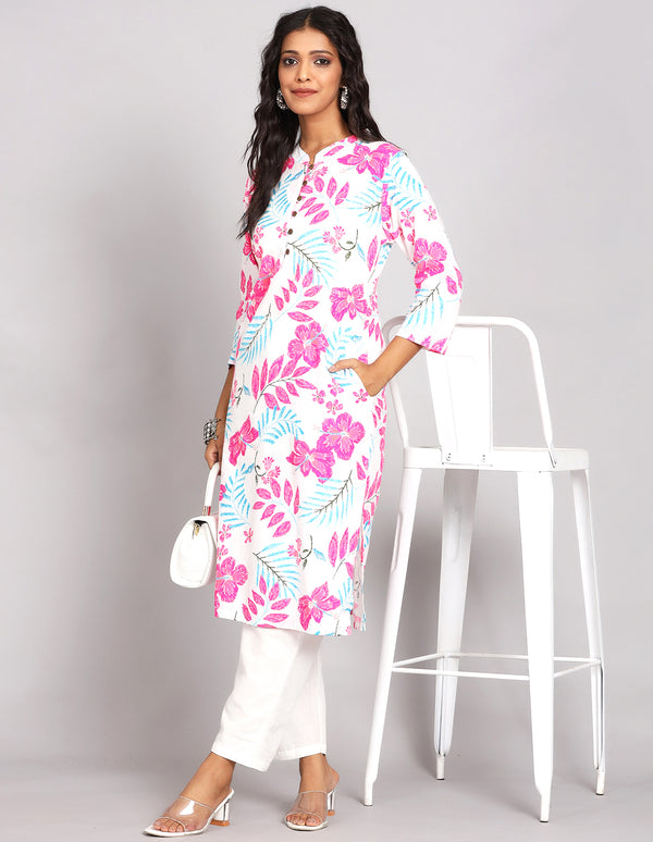 Stylish  White Long Kurti With Floral print, paired with white payjama and white transparent sandals, worn by a woman standing next to chair.