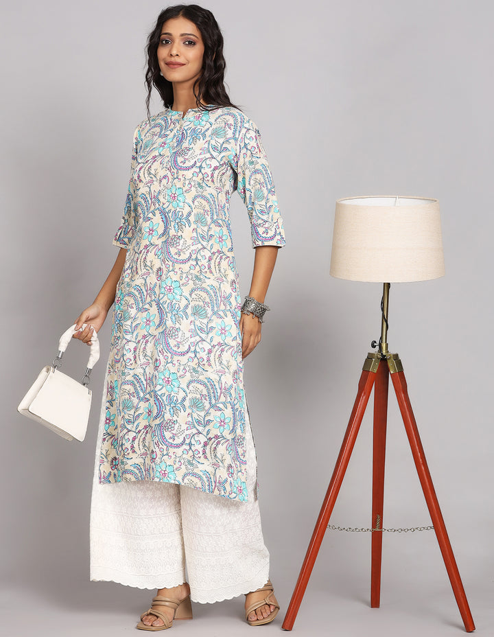 Stylish cream color long kurti with mandarin collar, paired with white palazzo and brown heeled sandals, worn by a woman standing next to lampstand with a white handbag.